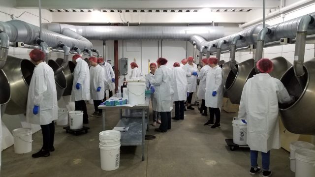Attendees in white coats and hairnets in a panning room