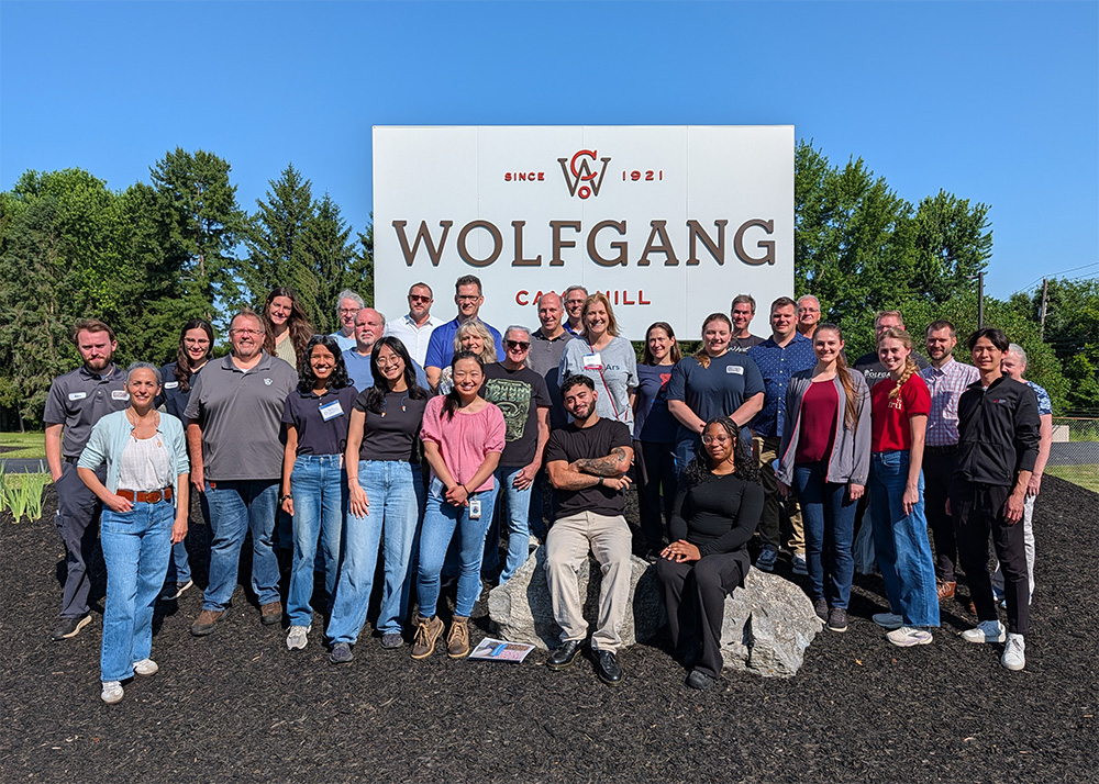 Group photo edit group of attendees and instructors outside on a sunny day in front of Wolfgang sign